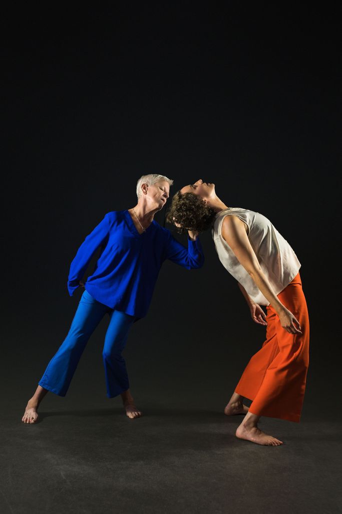 The dancers are in a supportive, weight sharing position. We see the side of Helen’s body as she archers backwards. Linda’s hand is at the back of Helen’s head supporting her in this arched back position. Linda’s stance leans in the direction of Helen, as she takes her weight. Linda looks towards Helen’s head, as of taking care to support her.