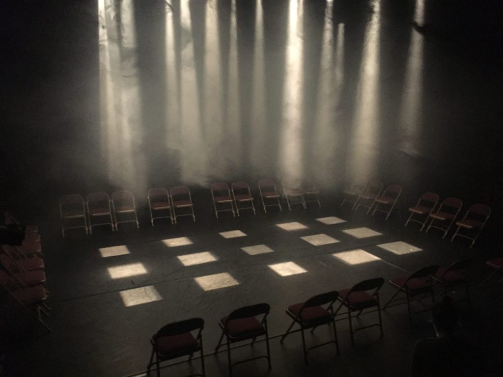 This Image is of an empty stage, before the audience arrive. Chairs are places around the edge, as the audience are on stage with Helen, and she moves around them. In the centre there are 15 beams of light shinning down. They are all dramatically highlighted by the misty haze in the room.