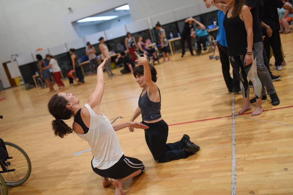 Image showing Helen teaching in Porto at the Inclusive dance festival, 'Meet, Share, Dance'. Helen is dancing with a participant. Both are on their knees and they face each other. Each of them reaches one arm high up in to the air; an echo of each others. movement. 