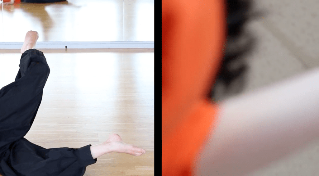 Image shows a frame from the film. It is a split screen. On the left-hand side, we can see just Helen's legs and feet. She is lying on the floor with one of her legs on the floor and one of her legs up in the air. On the right hand side of the picture, the other image is blurred. It is taken from a low viewpoint and we just see the blur of orange off Helen's T-shirt and the blur of brown of her curly hair. 